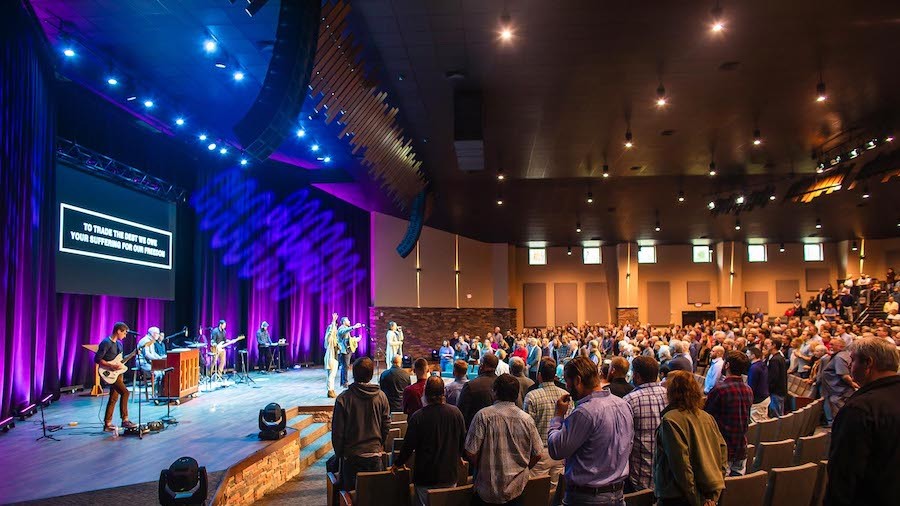 A church service with an LED video wall on the stage displaying song lyrics.