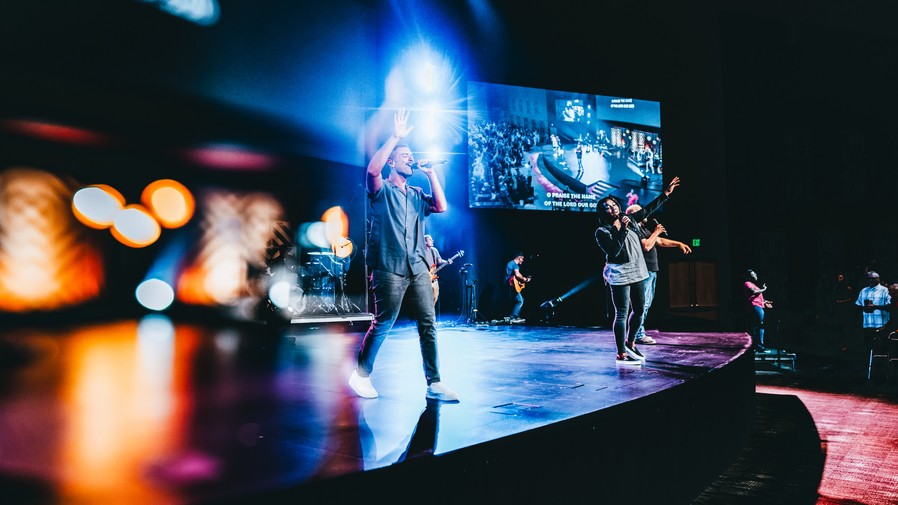 People singing into wireless microphones on the stage in a contemporary church.